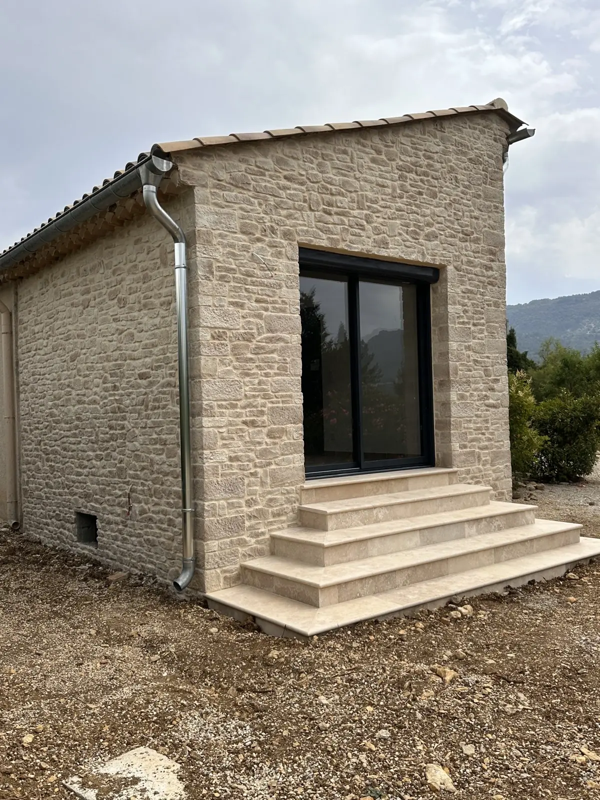 Annexe en pierre de parement vue d’angle, gouttière en zinc, collines au fond