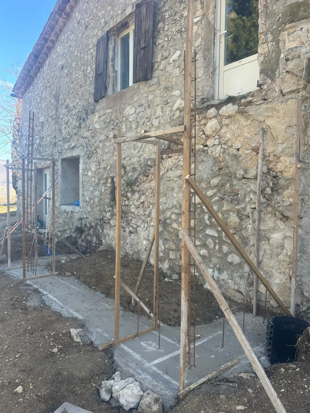 Pied d’une façade en pierre : semelle coulée avec ses fers d’attente, étais et bois de coffrage dressés