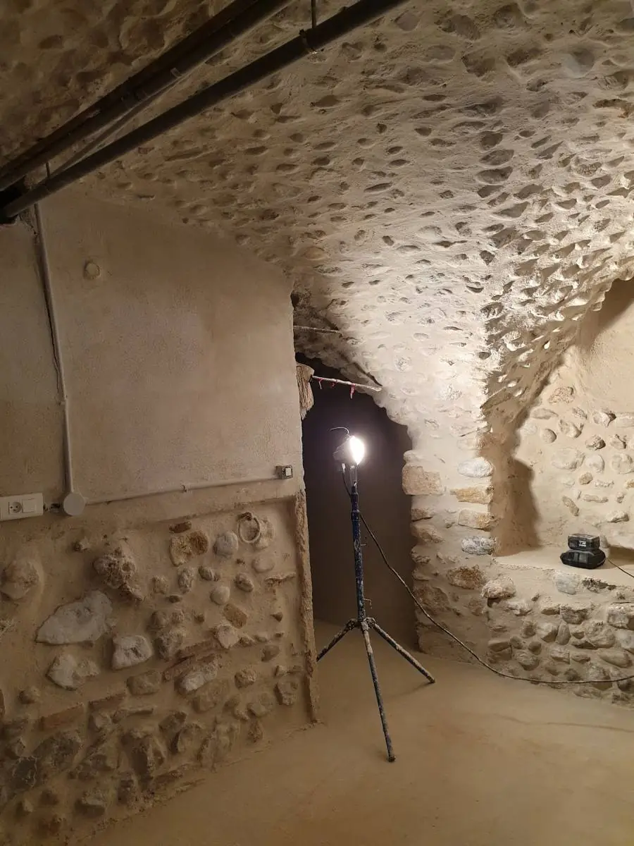Cave voûtée en pierre en travaux, projecteur sur trépied, mur bas en pierre