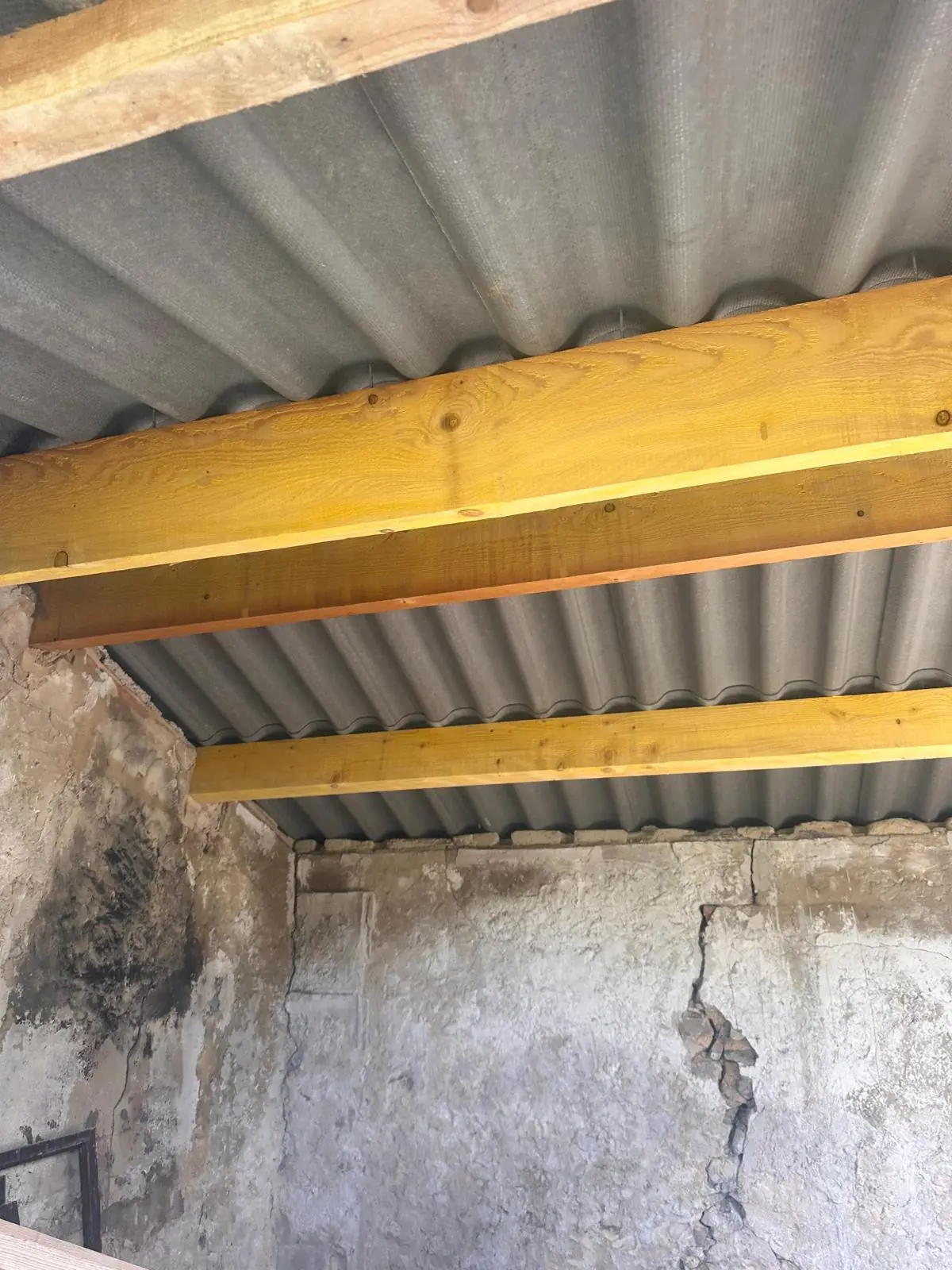 Charpente neuve en bois sous des plaques ondulées, mur fissuré à reprendre