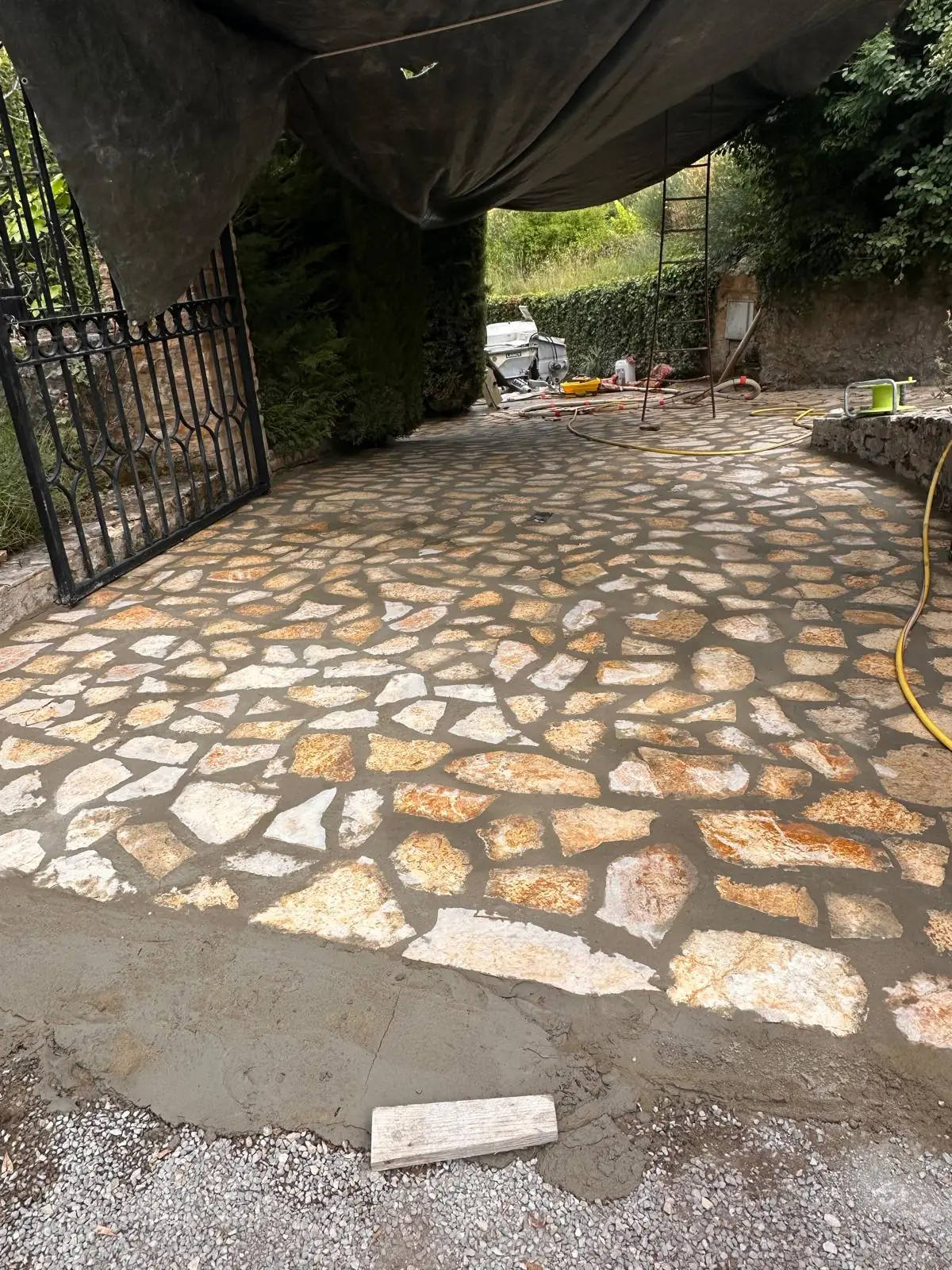 Cour en pierres plates jointoyées, portail en fer forgé ouvert