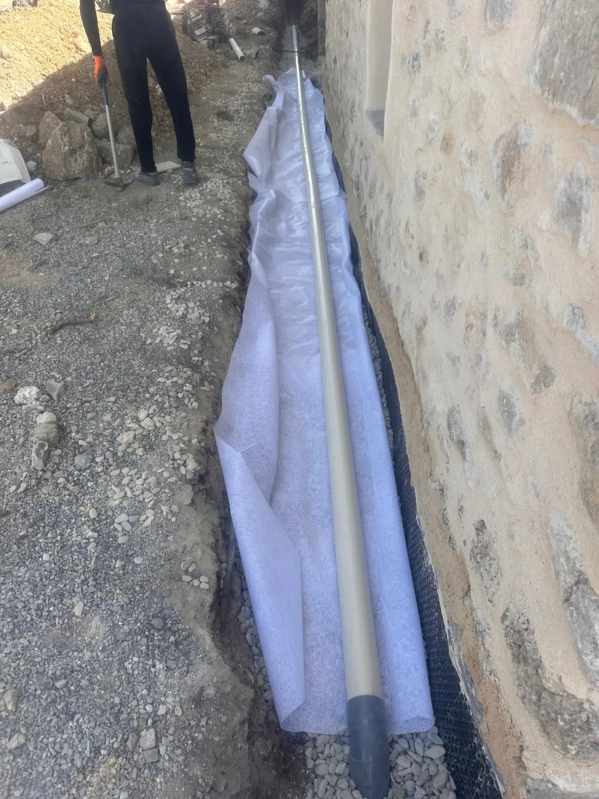Drain enveloppé de géotextile au fond d’une tranchée, le long d’un mur en pierre