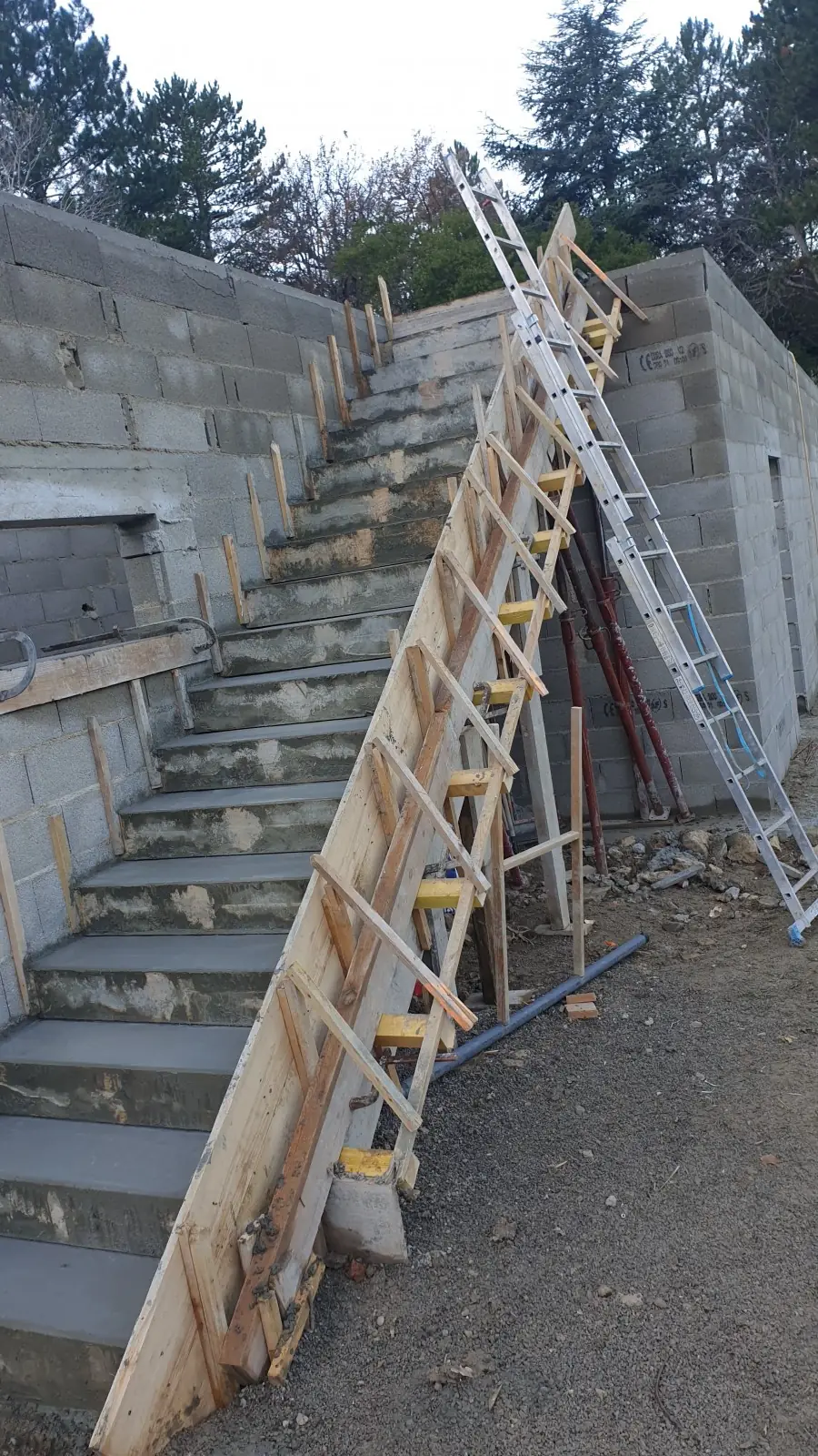 Escalier extérieur en béton décoffré le long d’un mur en blocs, échelle posée