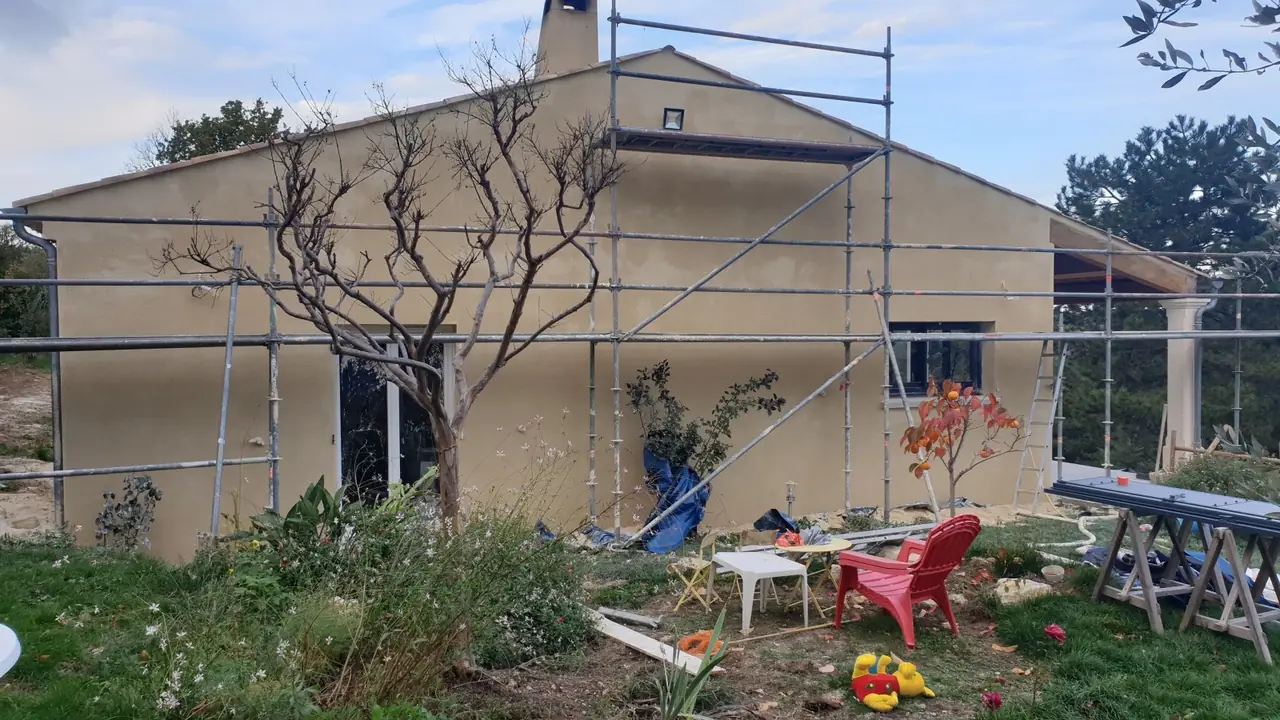 Maison enduite ocre sous échafaudage, jardin devant