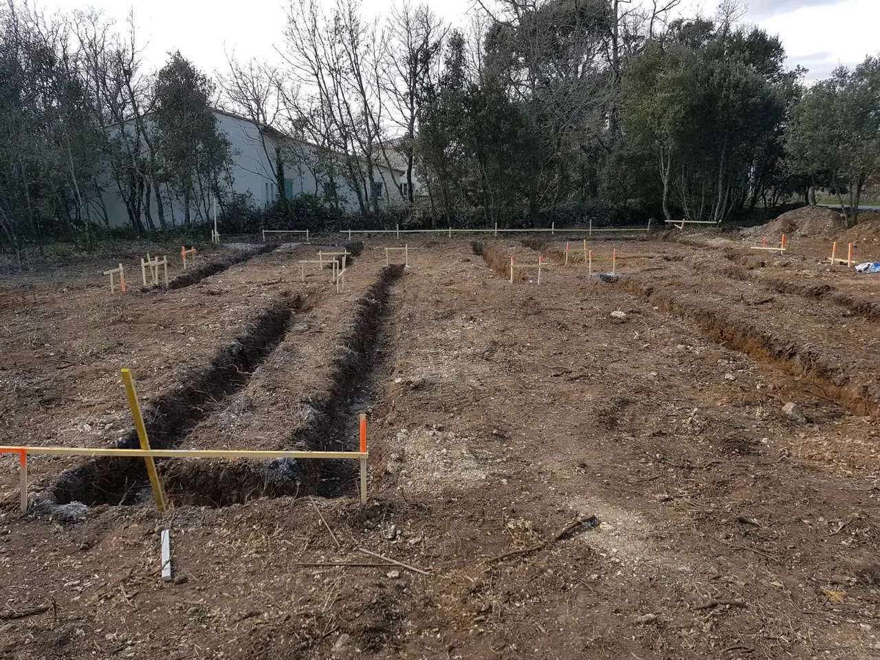 Terrain décapé, tranchées de fondation ouvertes et piquets d’implantation