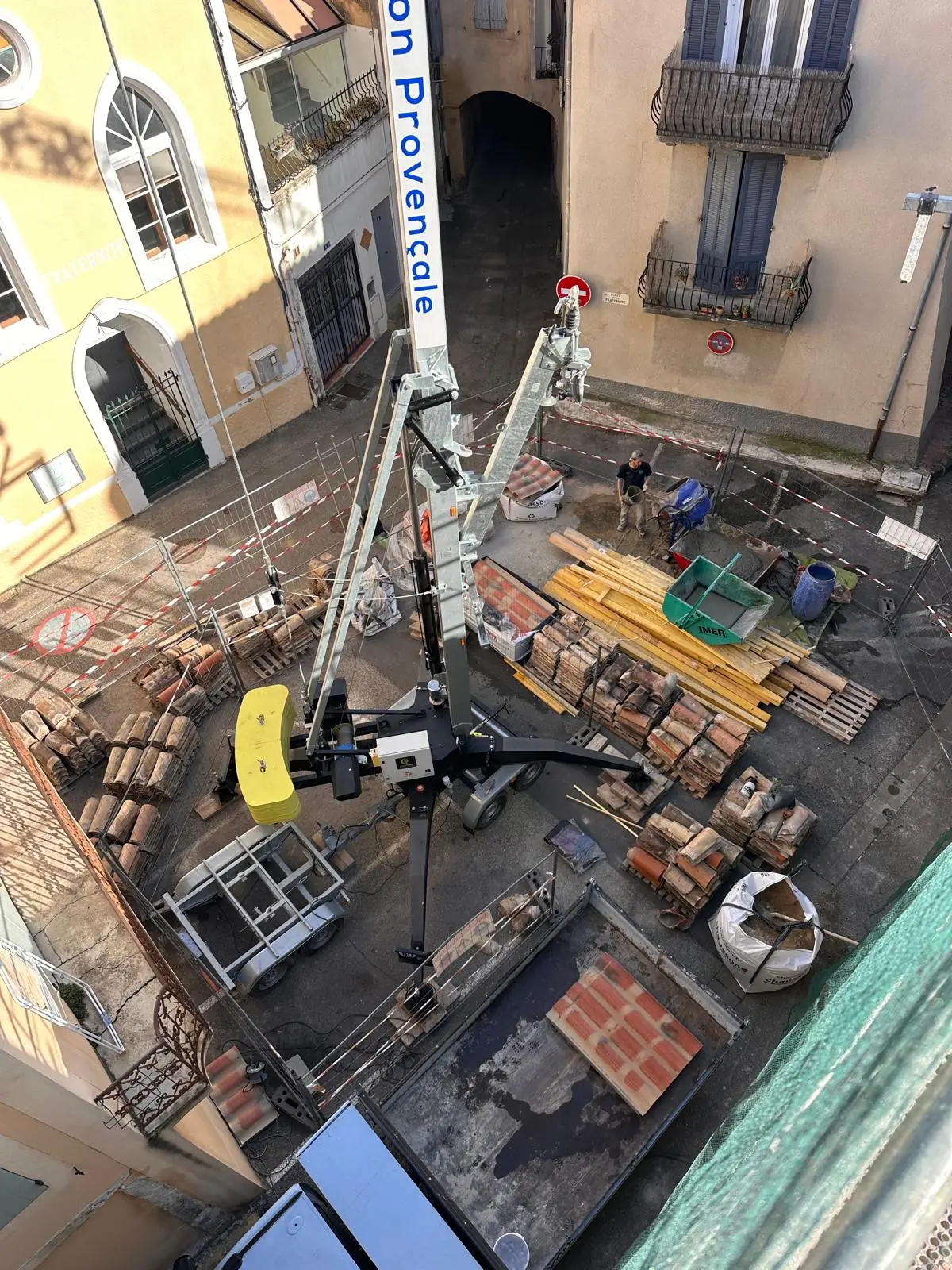 Grue de levage de l’entreprise montée dans une rue, tuiles et bois livrés au pied