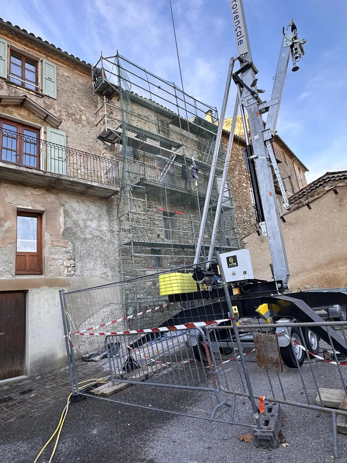 Immeuble en pierre sous échafaudage, grue de levage dans la rue, chantier balisé