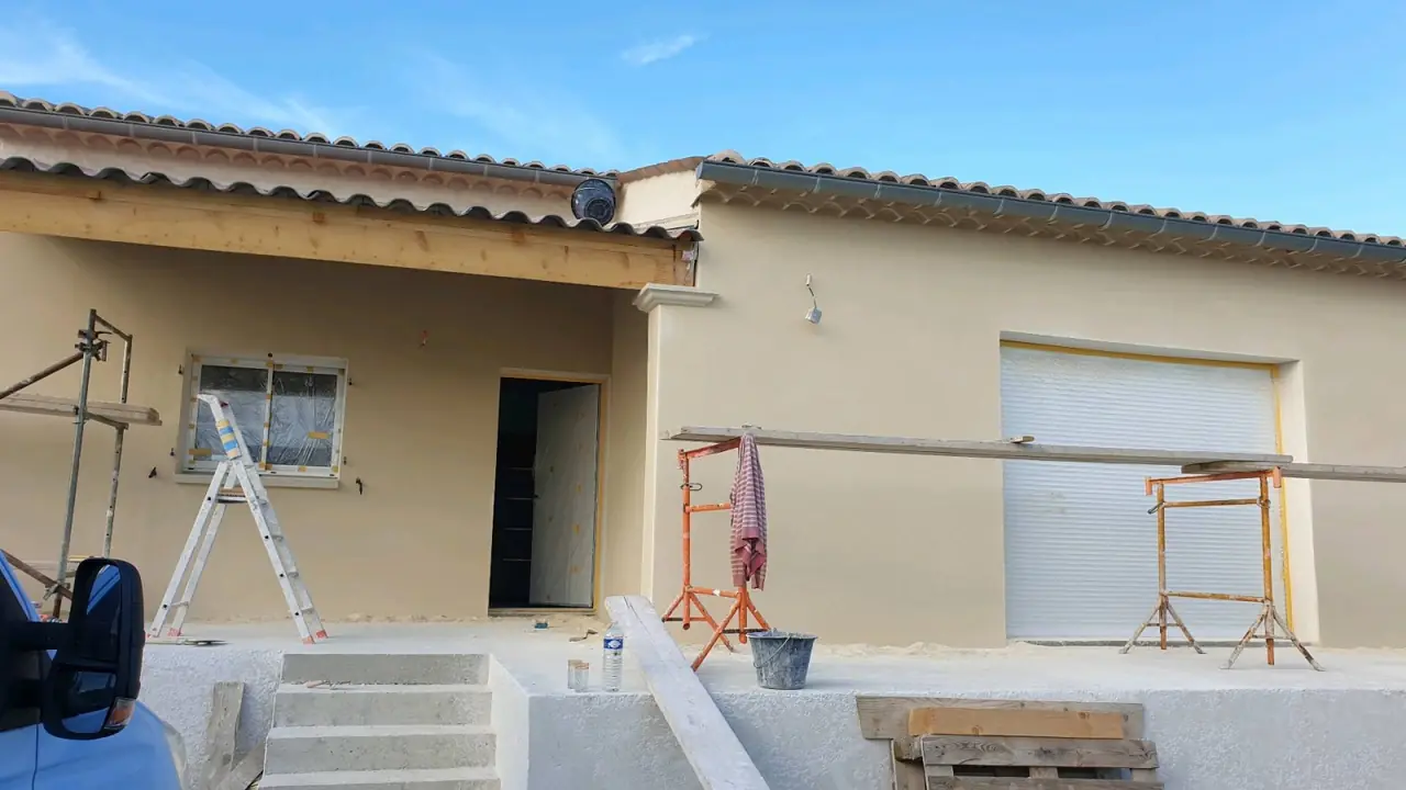 Maison enduite en fin de chantier : avancée de toit, porte de garage, escalier en béton, échafaudage léger