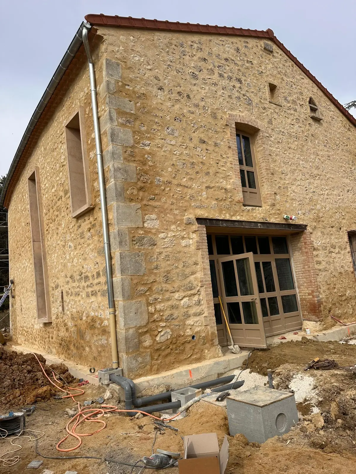 Maison en pierre aux joints refaits, chaînes d’angle et encadrements en pierre, abords encore en chantier