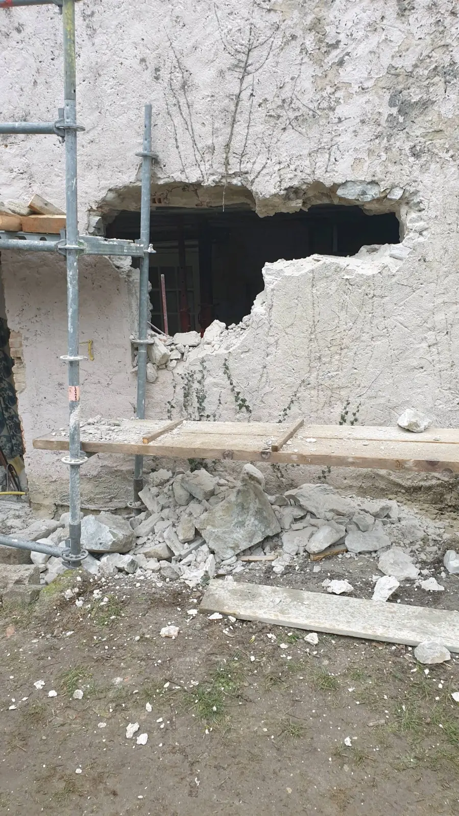 Mur enduit percé d’une ouverture en cours, gravats au pied, échafaudage