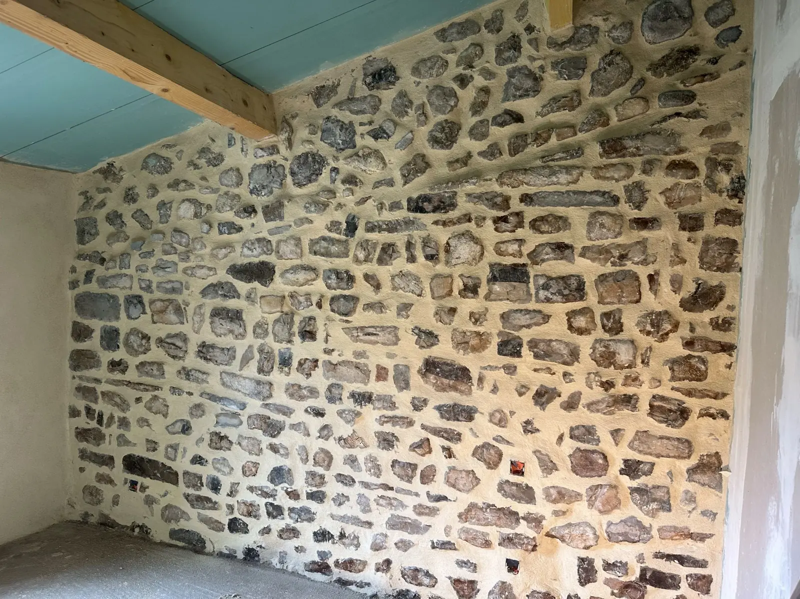 Mur intérieur en pierre apparente aux joints refaits clairs, plafond bleu-vert, poutre bois