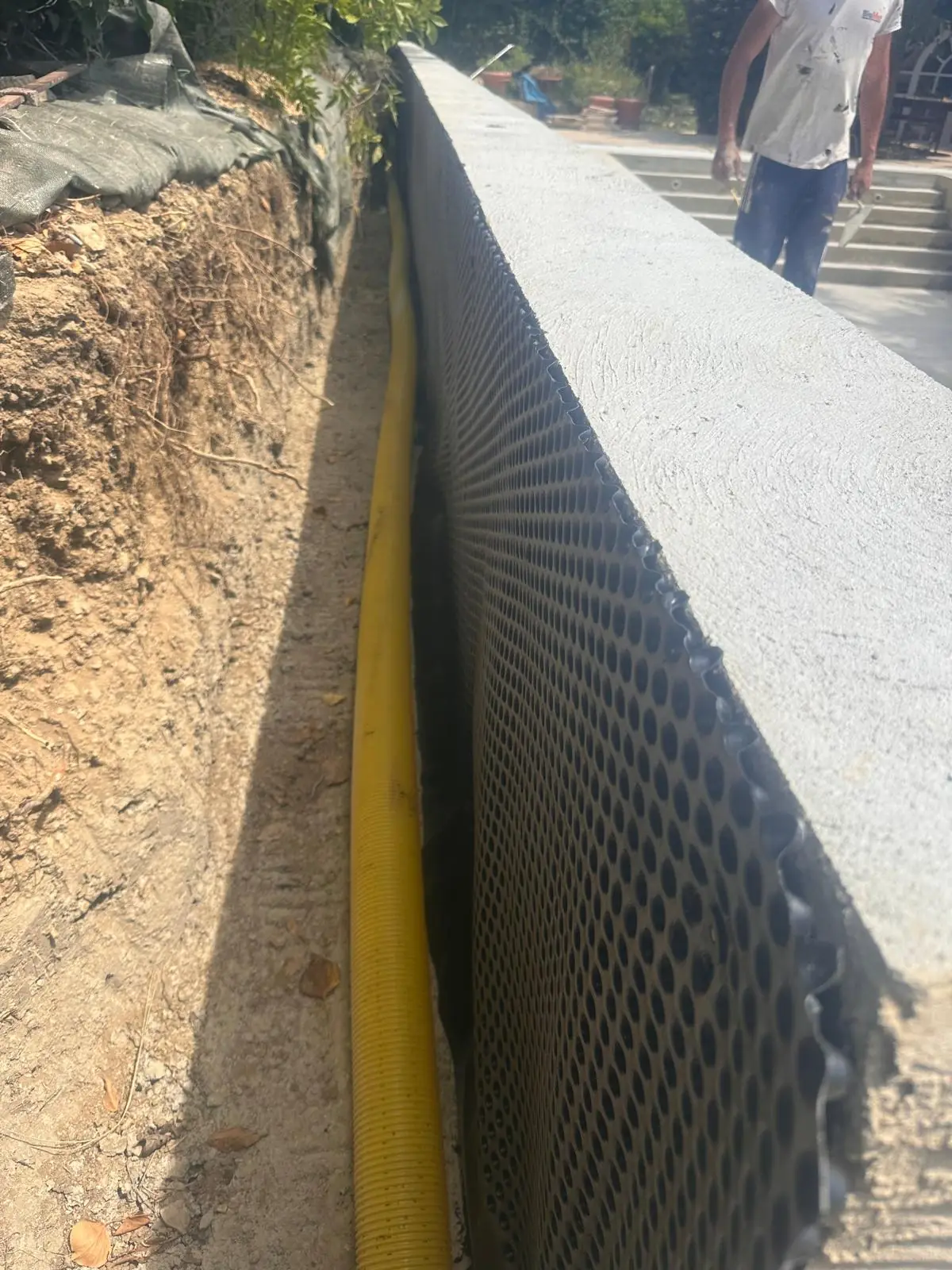 Mur enterré protégé par une nappe à excroissances, drain jaune au pied, dans sa tranchée