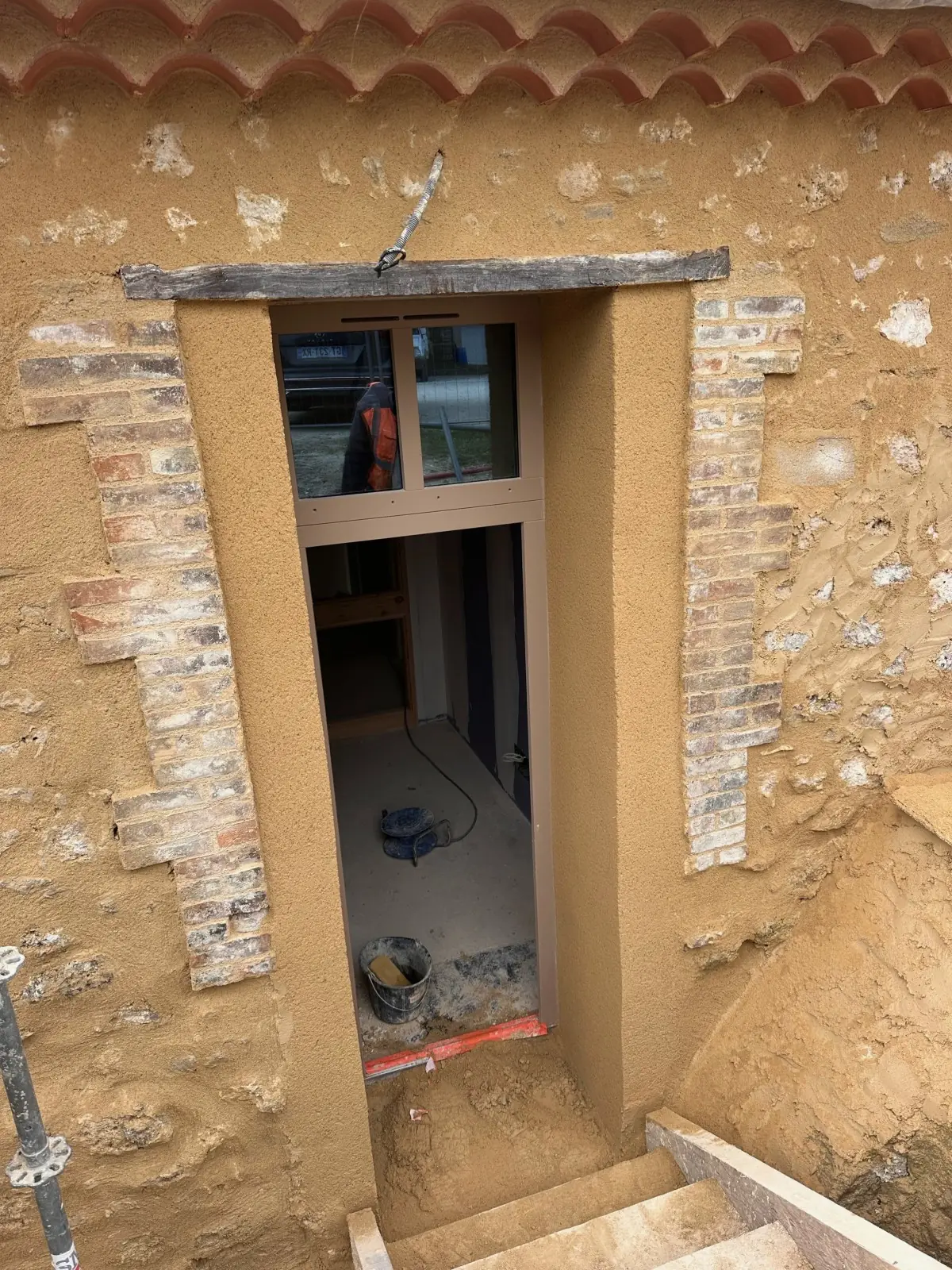 Porte dans un mur de pierre : encadrement en briques, linteau, enduit ocre autour, génoise au-dessus