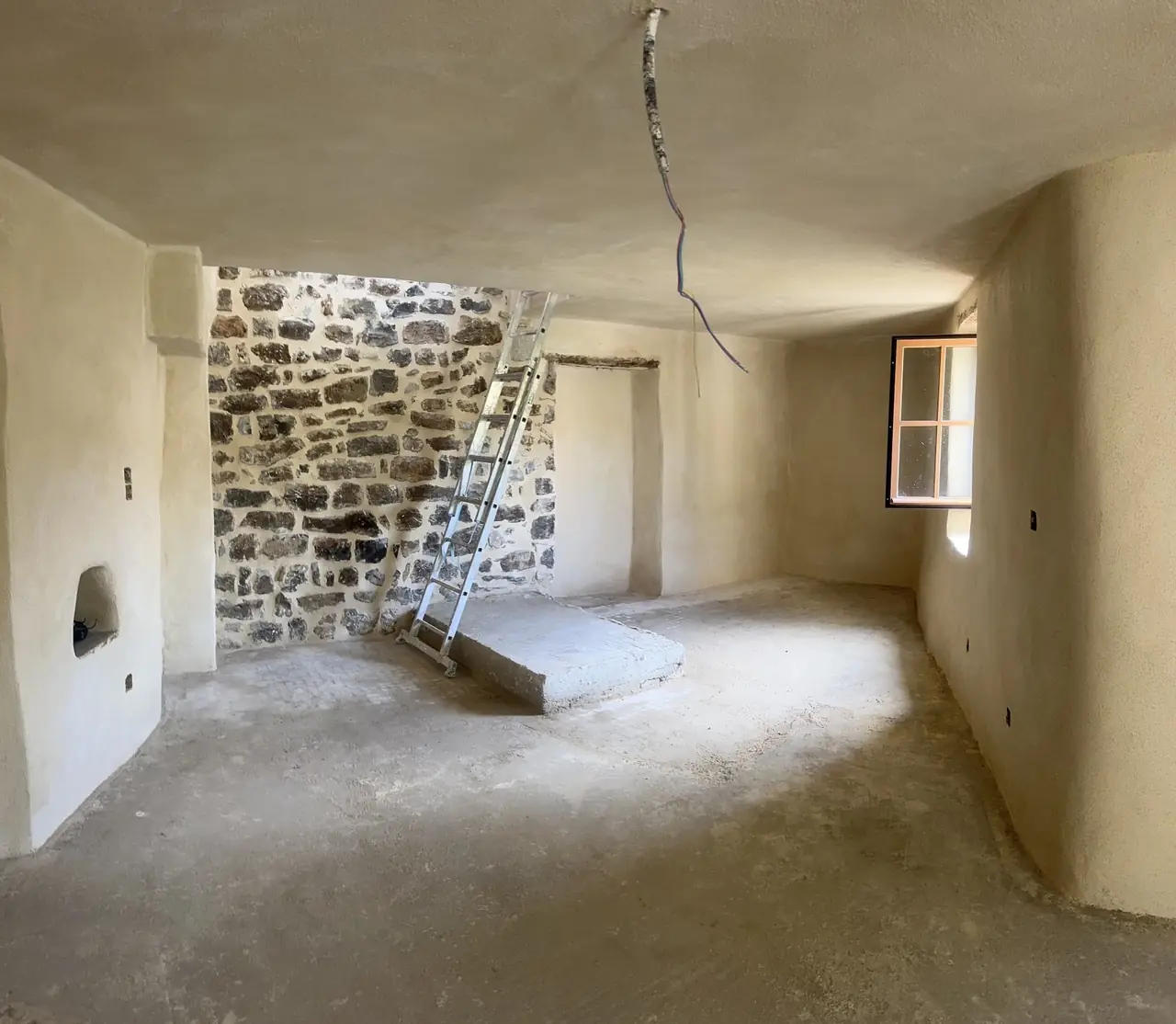 Pièce enduite avec un mur du fond en pierre apparente, échelle, sol brut