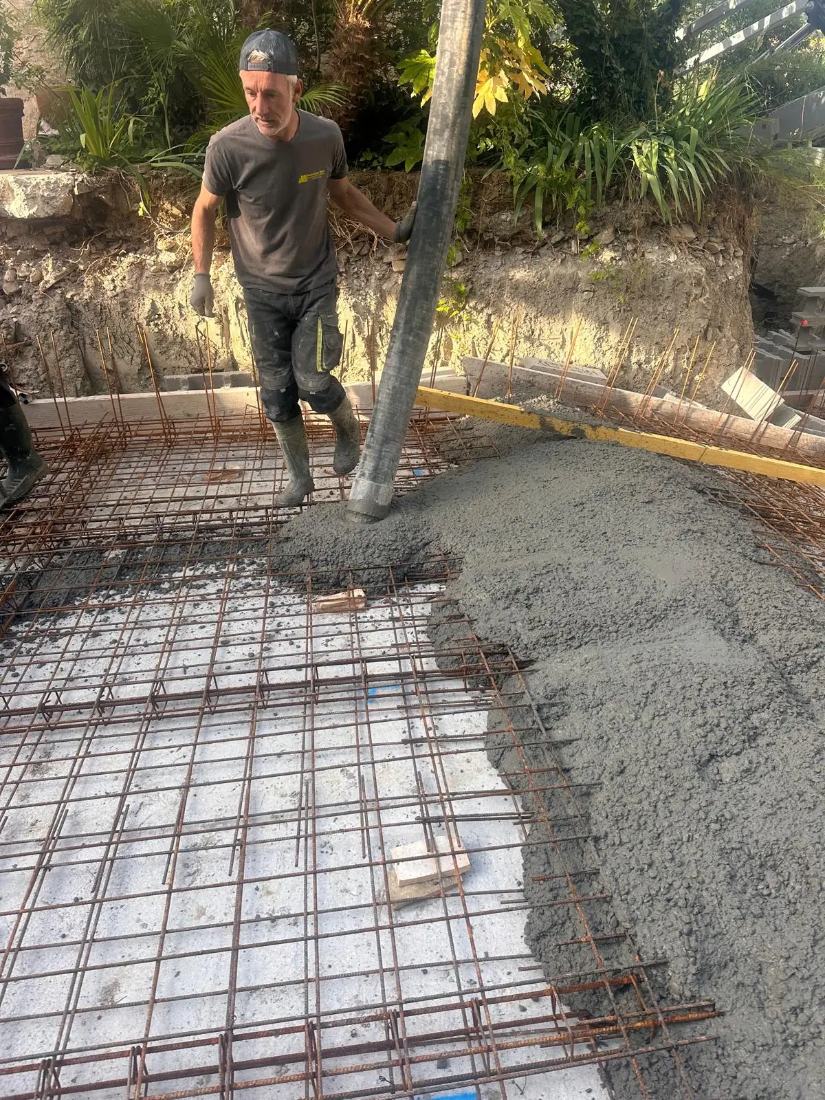 Coulage du radier d’une piscine : le béton arrive par le tuyau de la pompe sur le ferraillage