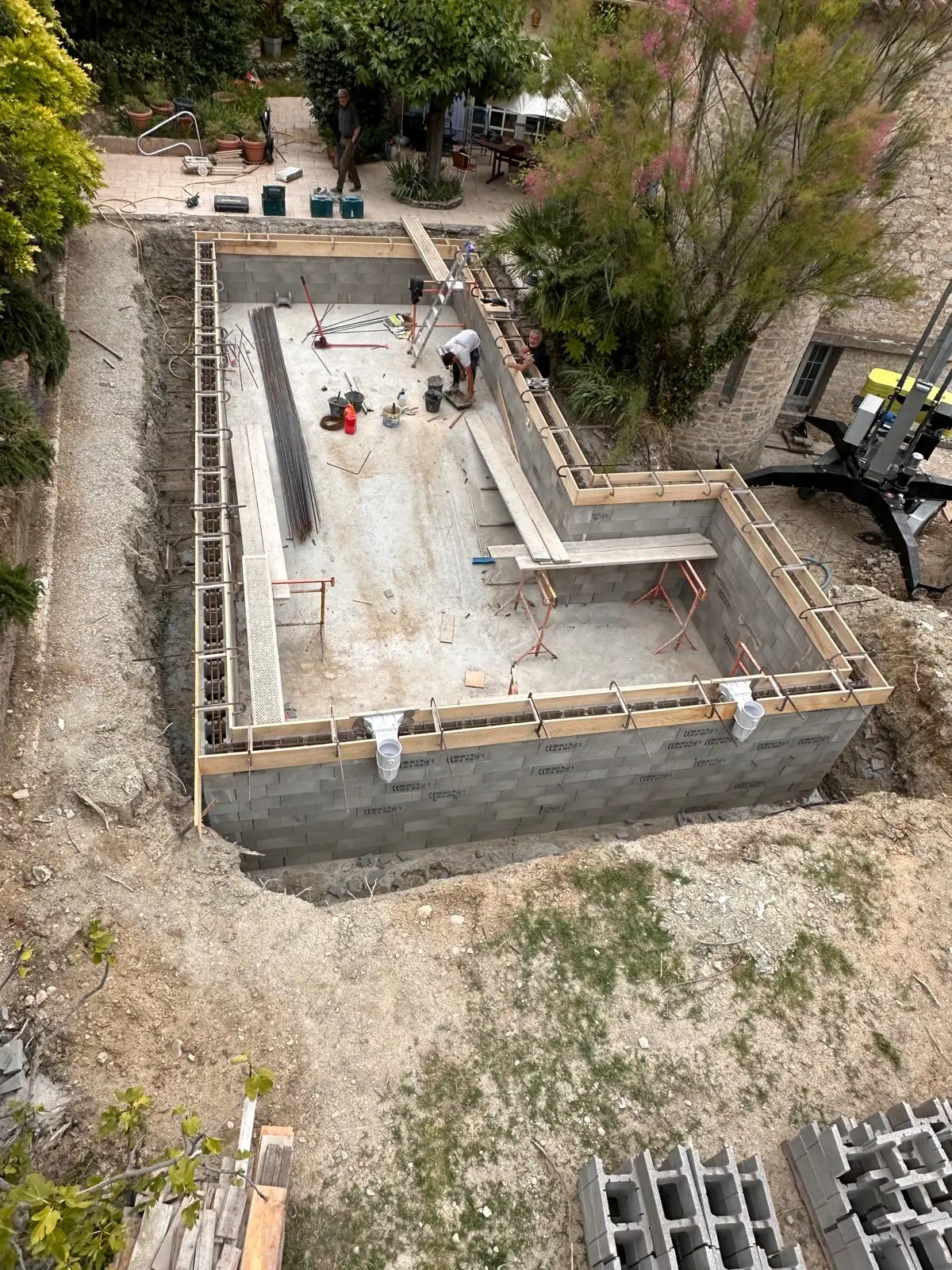 Piscine en L en construction vue d’en haut : murs en blocs à bancher sur le radier, coffrages en tête