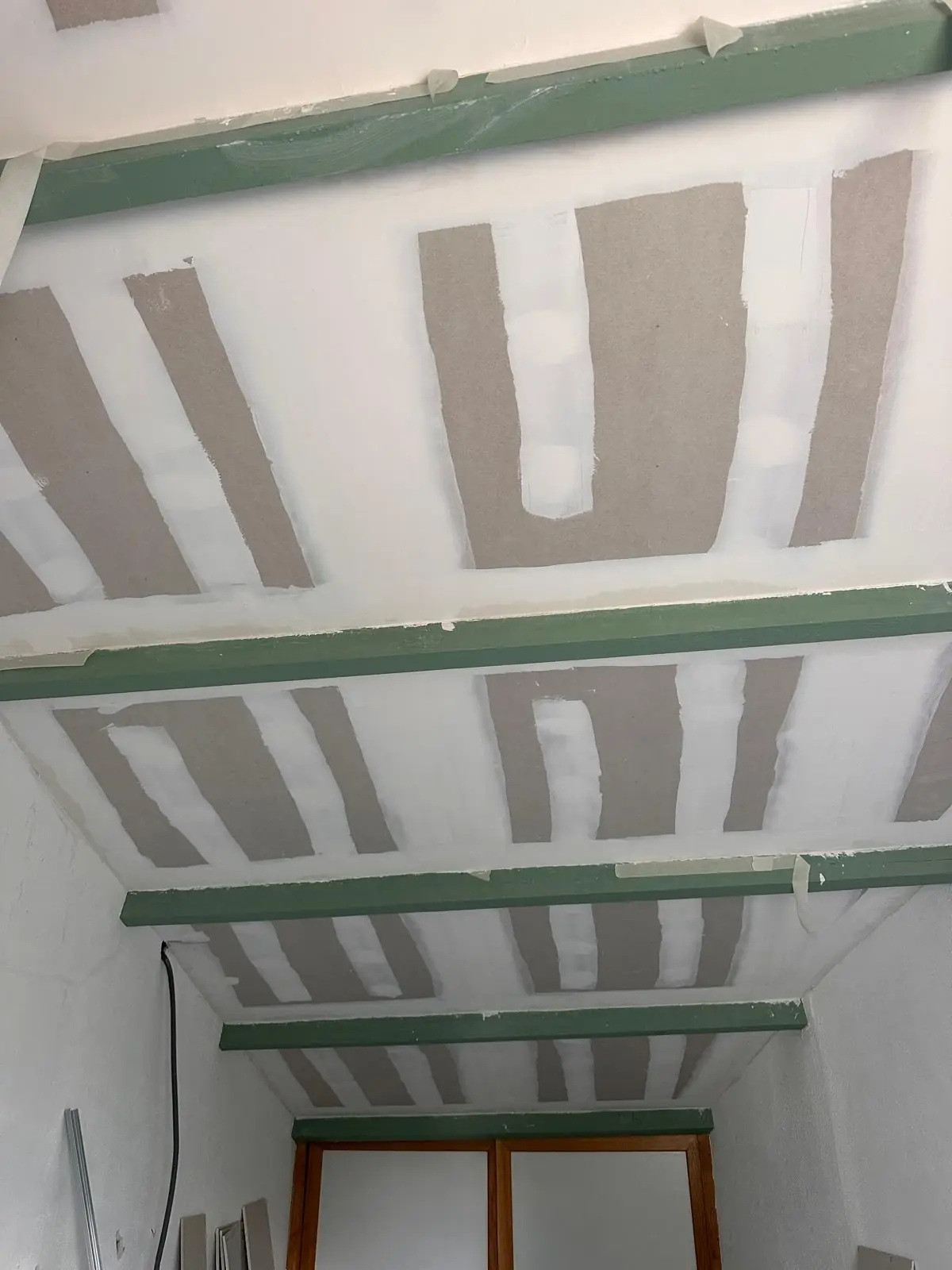 Plafond en plaques entre les solives, bandes et enduit en cours, menuiserie au fond