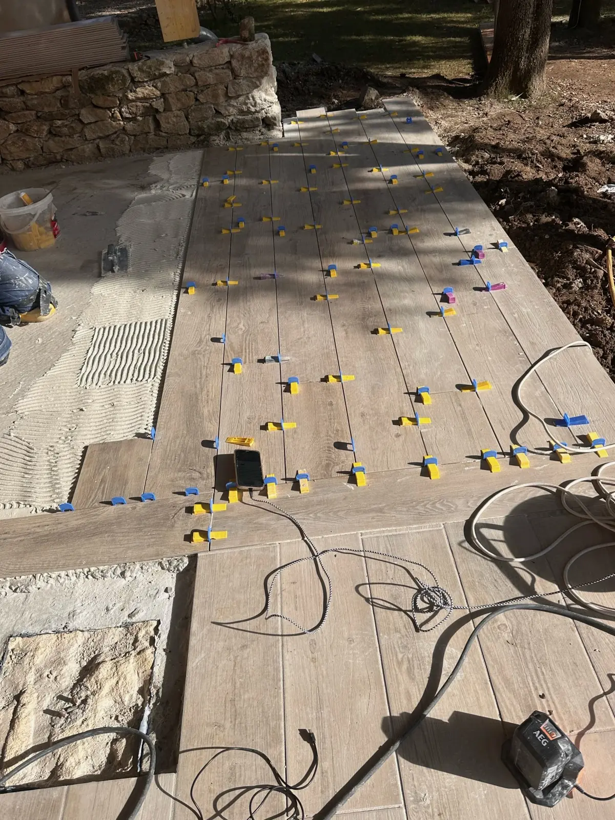 Pose en cours d'une terrasse en grands carreaux imitation bois, croisillons et cales de nivellement
