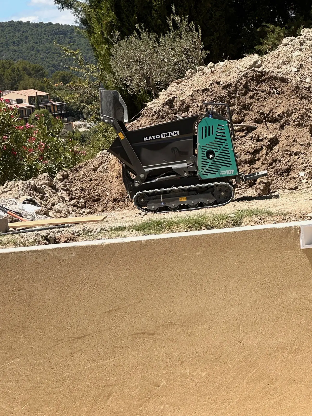 Mini-dumper chenillé au bord d’une fouille, mur enduit au premier plan