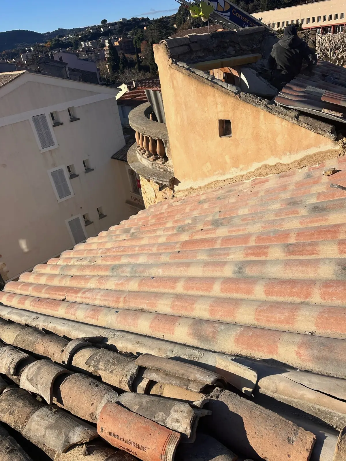 Toiture en tuiles canal d’une maison de village enduite ocre, vue d’en haut, immeubles autour