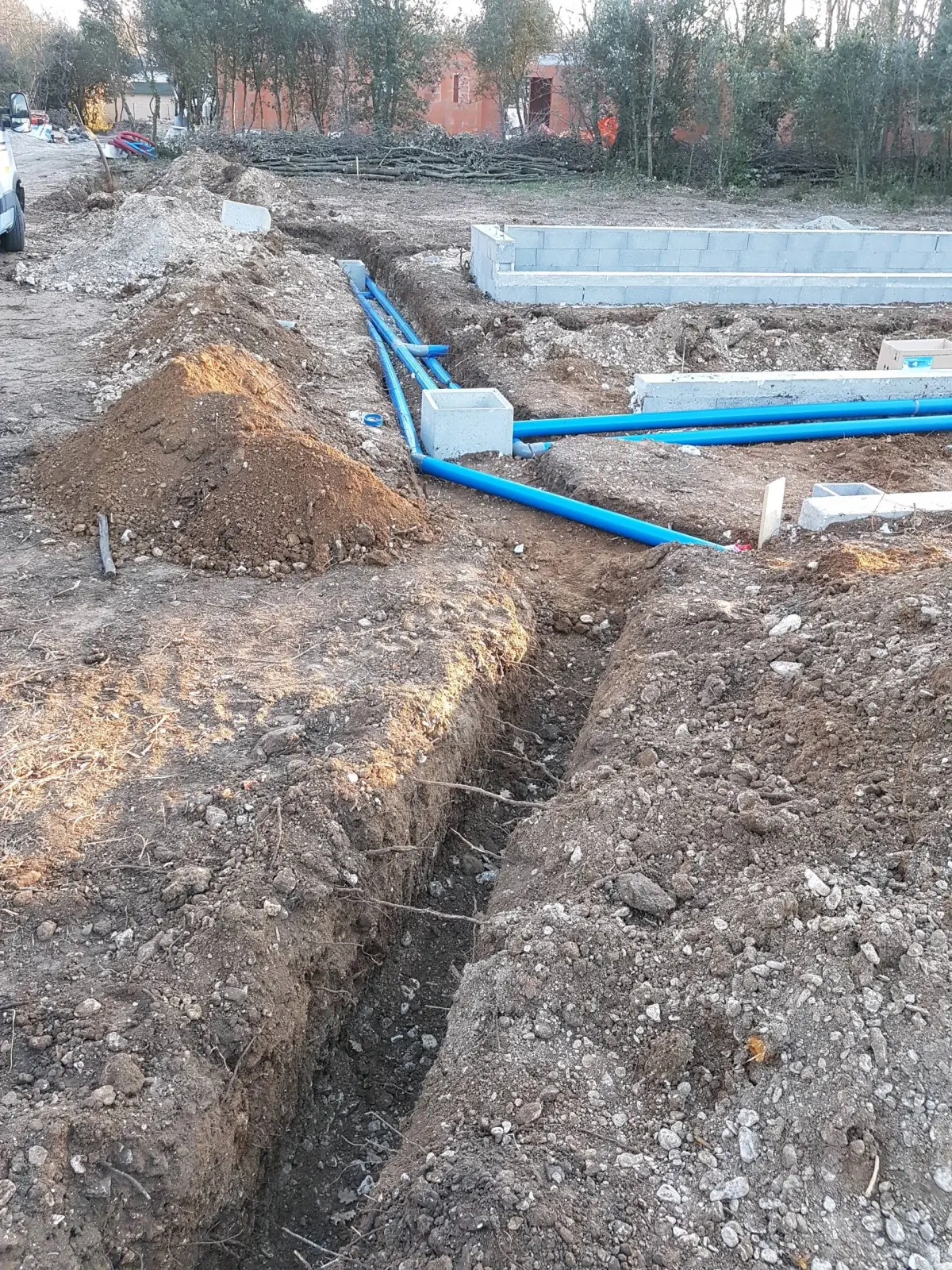 Tranchée ouverte avec les gaines bleues des réseaux, murs en blocs au fond