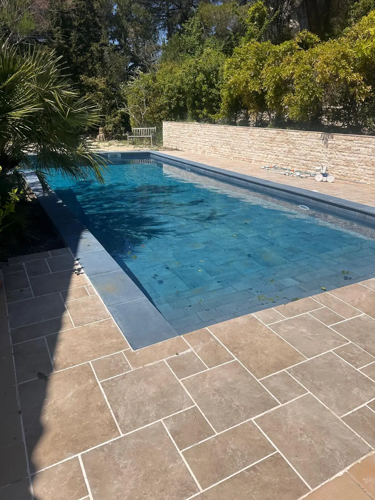 Piscine terminée vue d’un angle : margelles grises et grande plage en dallage ton pierre