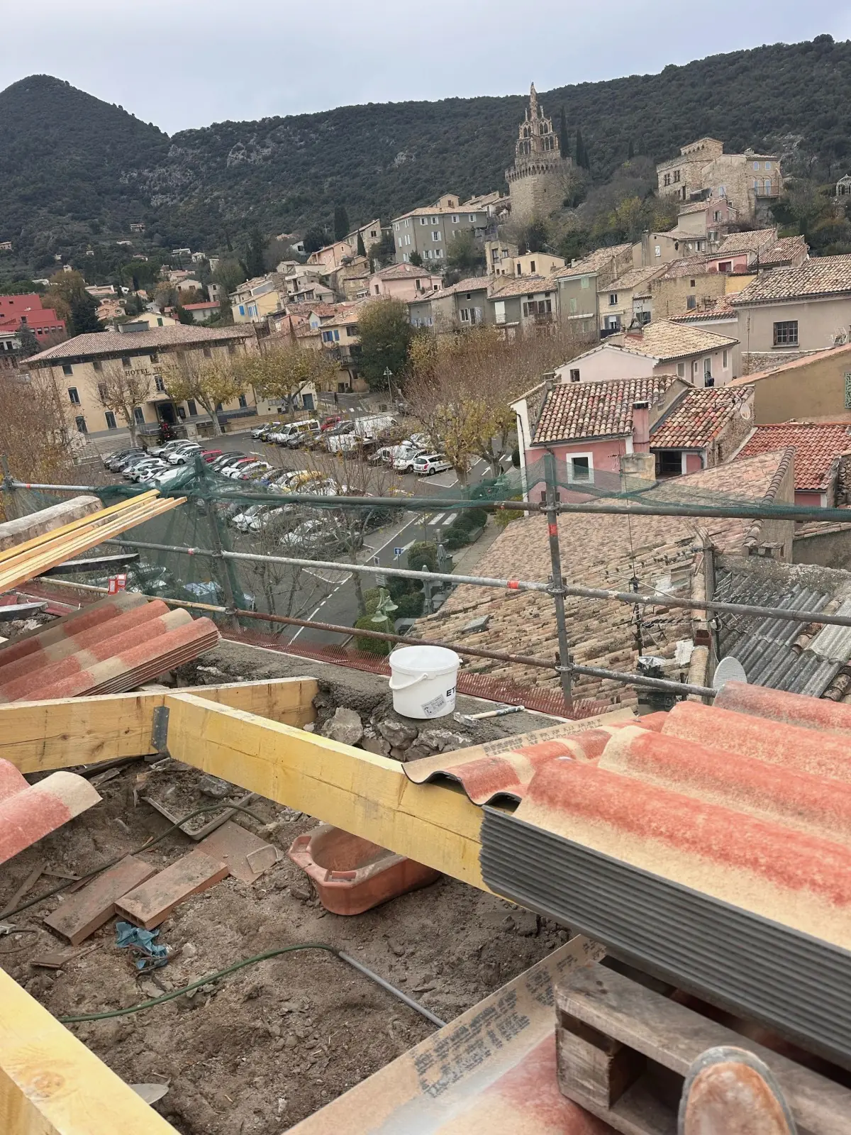 Toiture en tuiles canal en cours de réfection au-dessus d’un village, échafaudage, clocher au fond